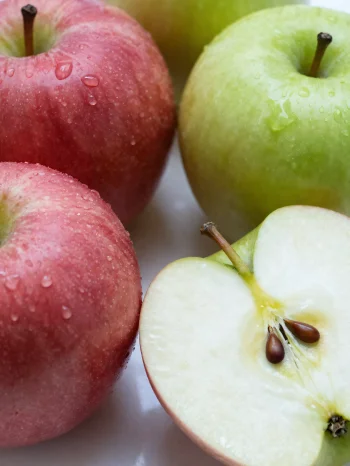 Manzanas rojas y verdes frescas en tabla de cortar, rebanadas y enteras, con jugo de manzana