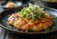Okonomiyaki con aceite de chile servido con salsa okonomiyaki y hojuelas de bonito
